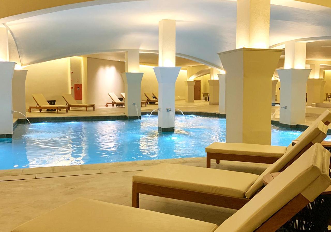 Buona Vitta Gramado Resort & Spa By Gramado Parks Exteriör bild The photo shows an indoor spa or relaxation area with a tranquil atmosphere. There is a large swimming pool with clear blue water, illuminated by soft lighting. Surrounding the pool are several comfortable lounge chairs. The architecture features ele
