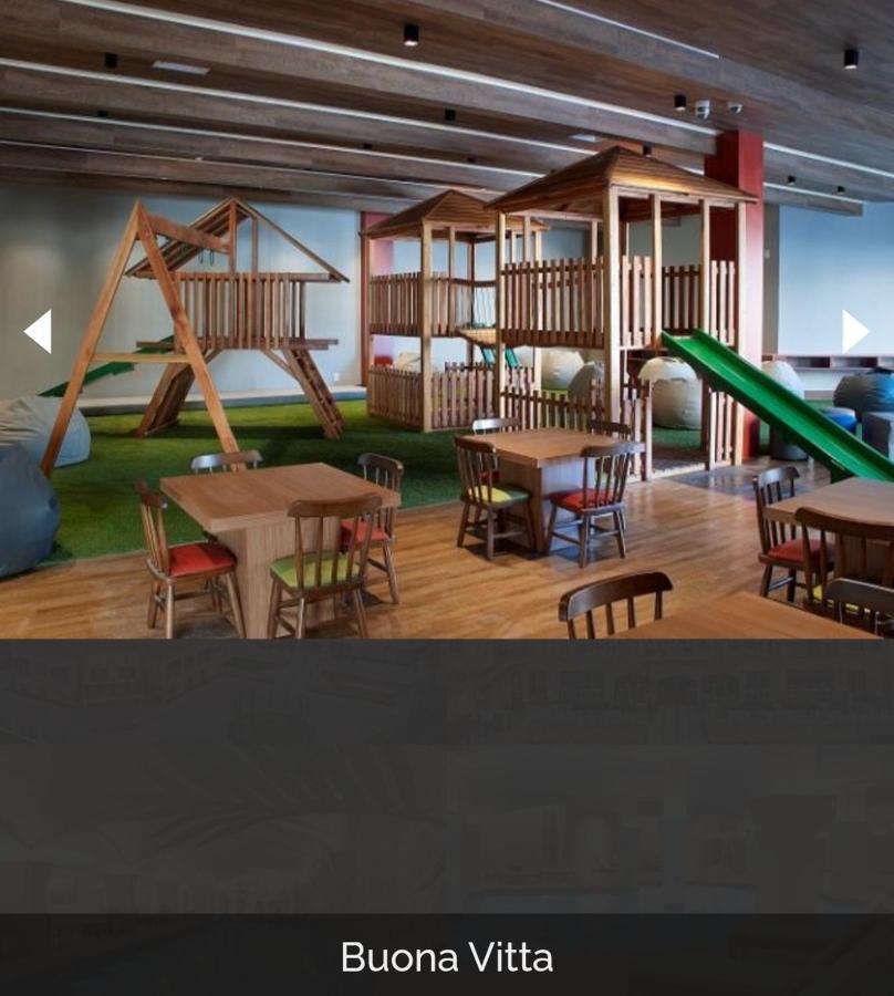 Buona Vitta Gramado Resort & Spa By Gramado Parks Exteriör bild The photo shows a play area designed for children, featuring a wooden play structure with slides and climbing areas. In the foreground, there are several small wooden tables and chairs arranged for seating. The floor is covered with green turf, resem