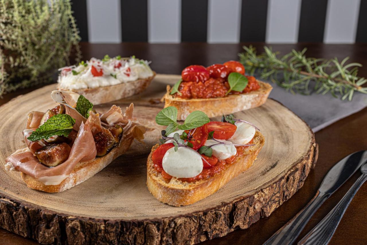 Buona Vitta Gramado Resort & Spa By Gramado Parks Exteriör bild The photo displays a wooden serving platter featuring four different types of bruschetta. Each piece of bruschetta is topped with various ingredients:

1. The top left has a creamy spread, possibly cheese or ricotta, garnished with fresh herbs and sm