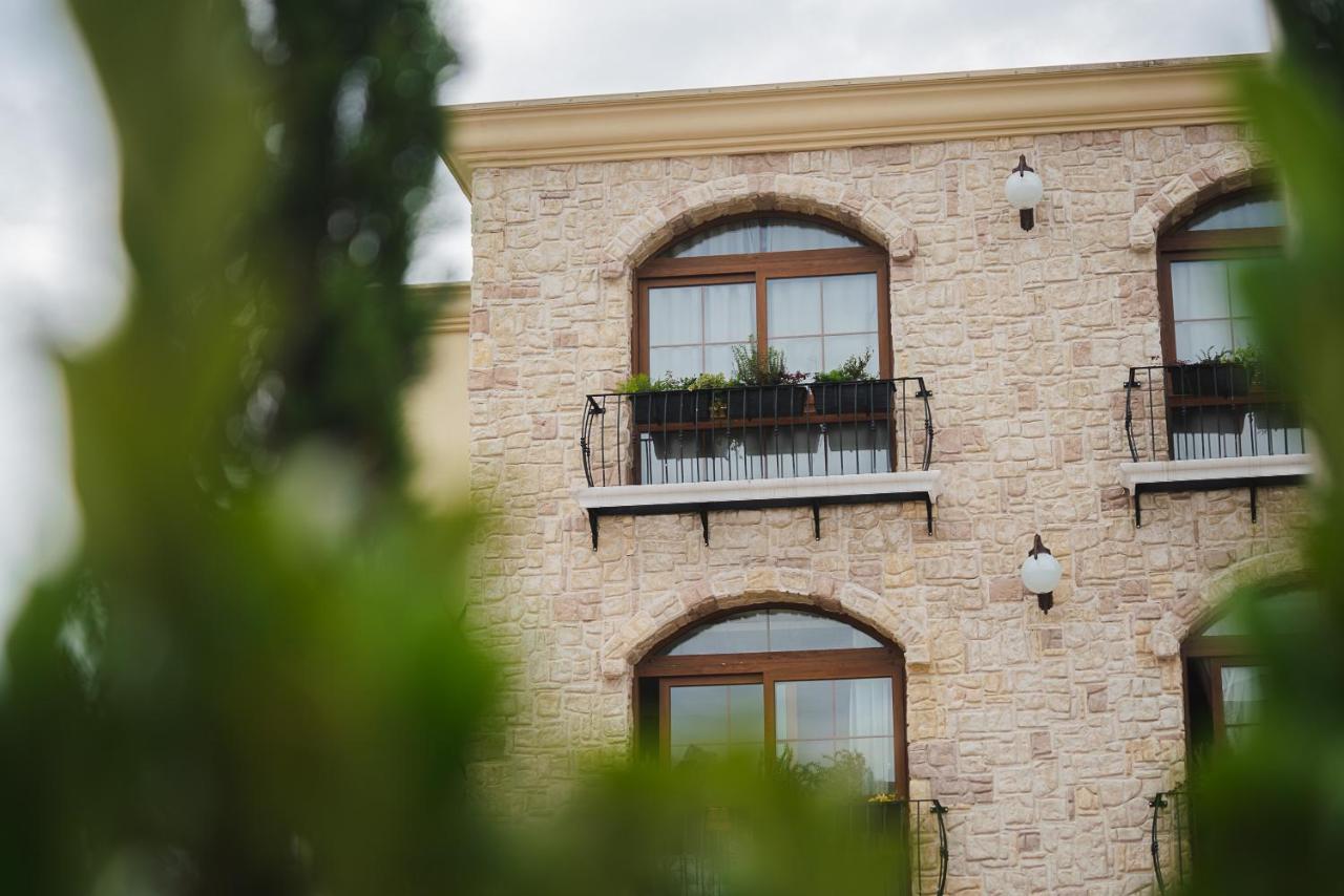 Buona Vitta Gramado Resort & Spa By Gramado Parks Exteriör bild The photo depicts a stone building with a textured exterior. It features several windows with wooden frames. Each window has a small balcony adorned with decorative plants. There are also wall-mounted light fixtures flanking the windows. In the foreg