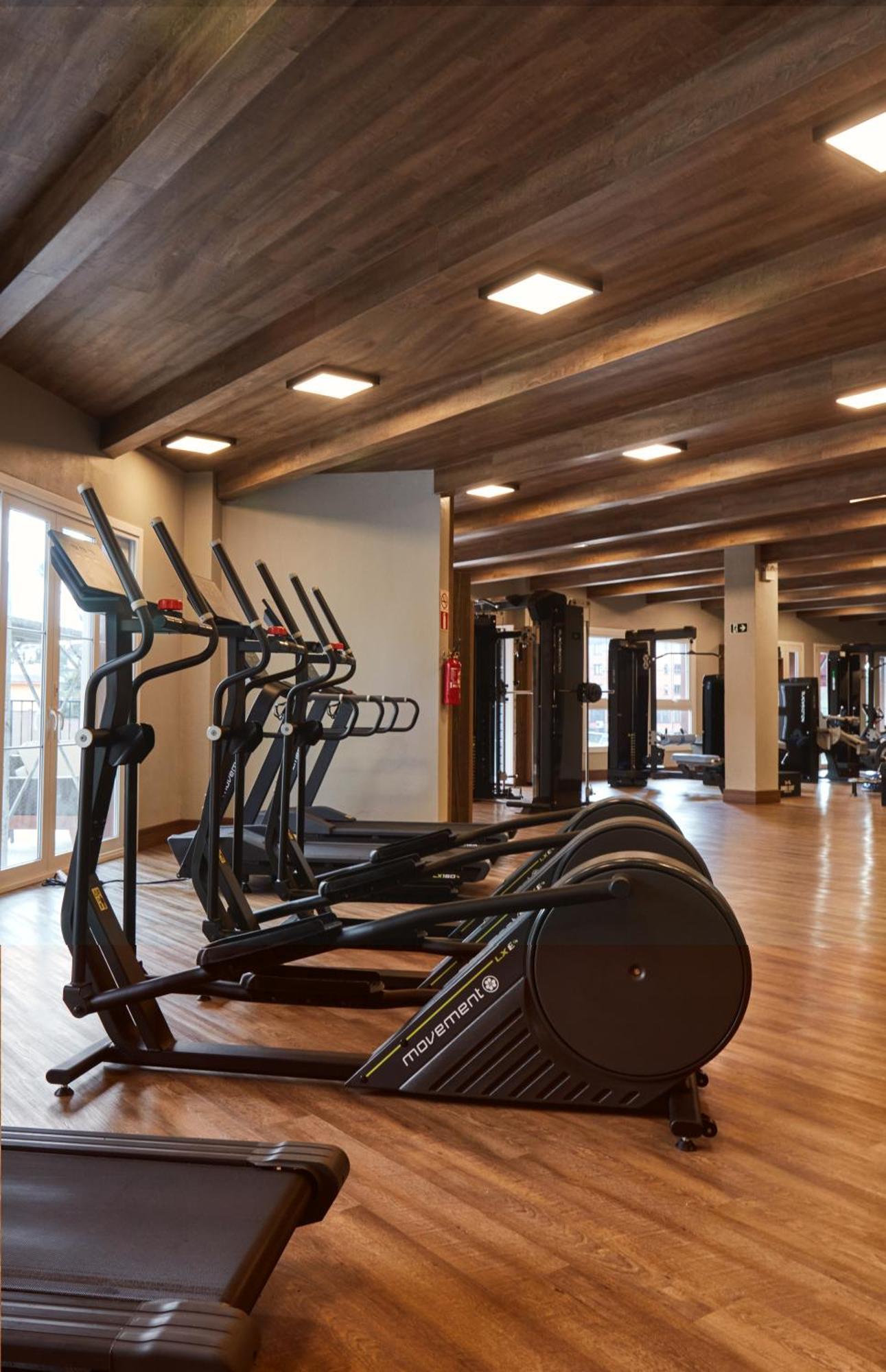 Buona Vitta Gramado Resort & Spa By Gramado Parks Exteriör bild The photo shows a modern gym interior with wooden flooring and a ceiling with wooden beams. There are several exercise machines, including elliptical trainers and a treadmill, positioned in the foreground. In the background, there are additional work