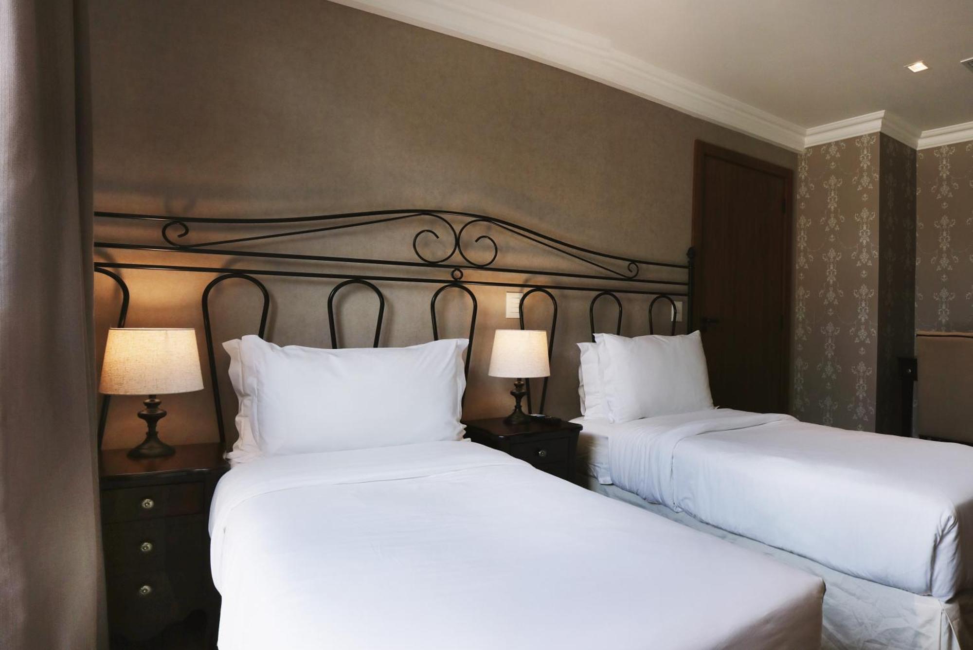 Buona Vitta Gramado Resort & Spa By Gramado Parks Exteriör bild The photo shows a neatly arranged hotel room featuring two single beds with white bedding. The beds have decorative metal headboards, and there are bedside tables on either side with lamps. The room's walls have a subtle design, and there is a door v