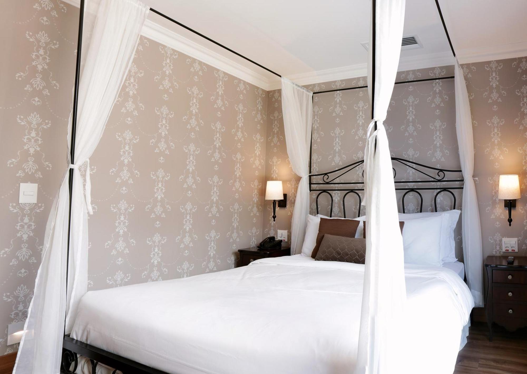 Buona Vitta Gramado Resort & Spa By Gramado Parks Exteriör bild The photo shows a elegantly decorated bedroom featuring a four-poster bed with white drapes. The bed is made with white linens and has some brown accent pillows. The walls are adorned with a subtle floral pattern, and there are two bedside lamps prov