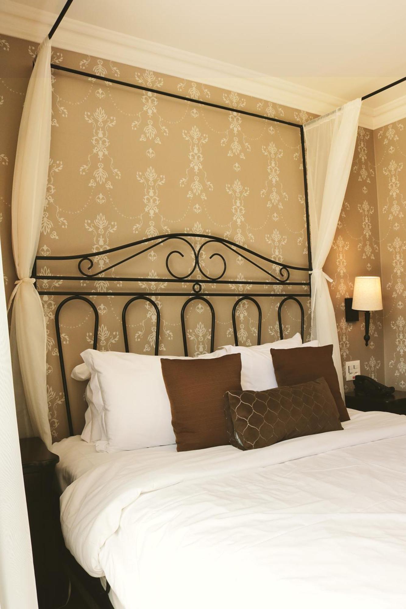 Buona Vitta Gramado Resort & Spa By Gramado Parks Exteriör bild The photo shows a cozy bedroom setup featuring a decorative metal bed frame with a scroll design as the headboard. The bed is adorned with several white pillows and two brown decorative cushions. The wall behind the bed is covered with a light-colore
