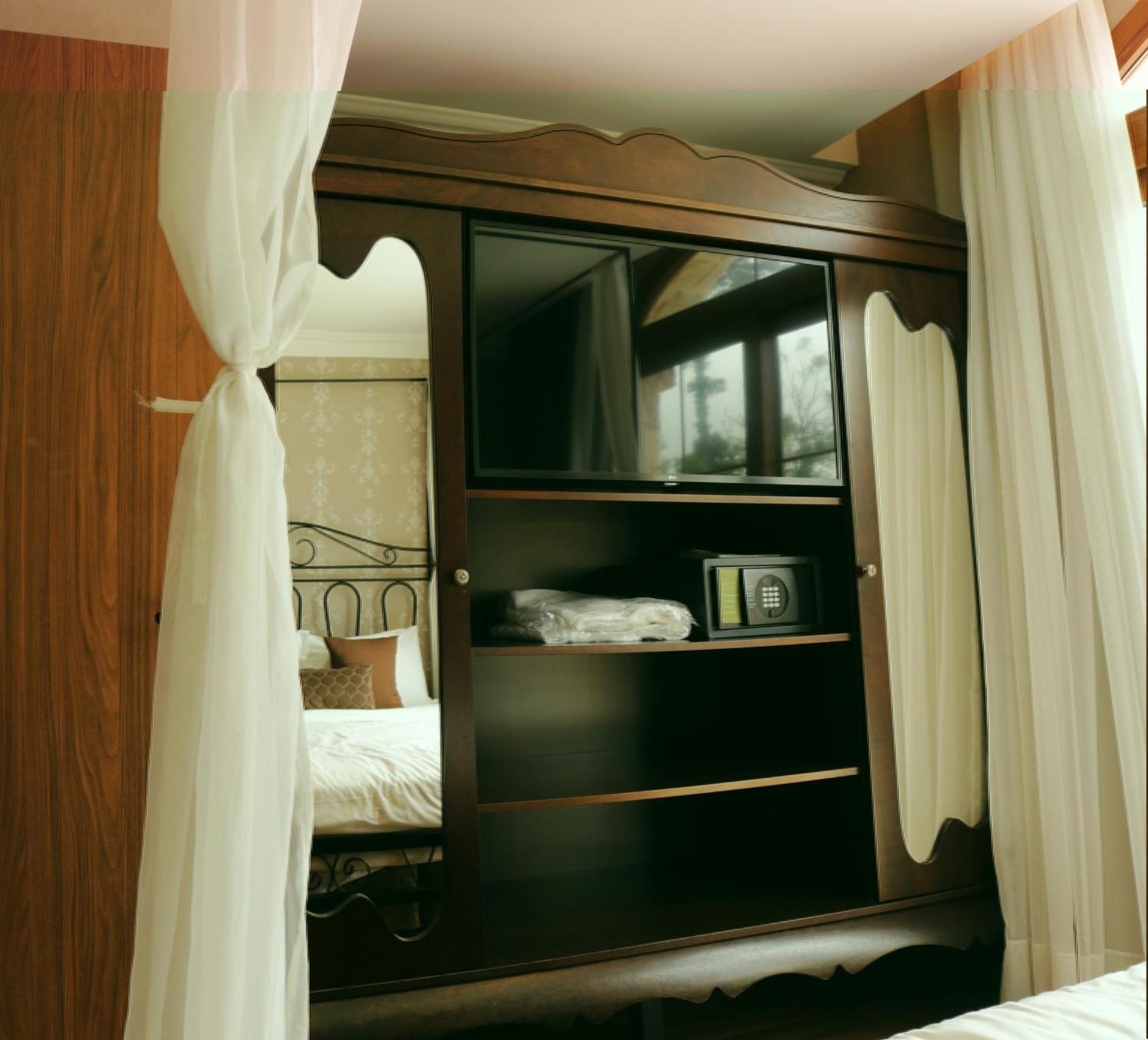 Buona Vitta Gramado Resort & Spa By Gramado Parks Exteriör bild The image shows a wooden cabinet with a television mounted on the front. The cabinet has decorative edges and is paired with sheer white curtains on either side. Inside the cabinet, there are shelves, and a small safe or storage box is visible on one