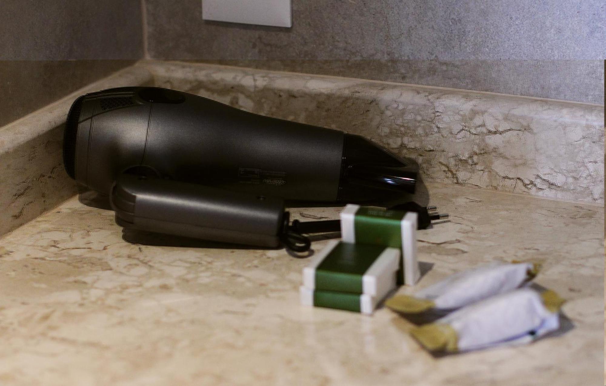 Buona Vitta Gramado Resort & Spa By Gramado Parks Exteriör bild The photo shows a black hairdryer placed on a marble countertop. Next to the hairdryer, there are two wrapped items, likely toiletries, with green and white packaging. Additionally, there are two more items, also wrapped, which appear to be in simila