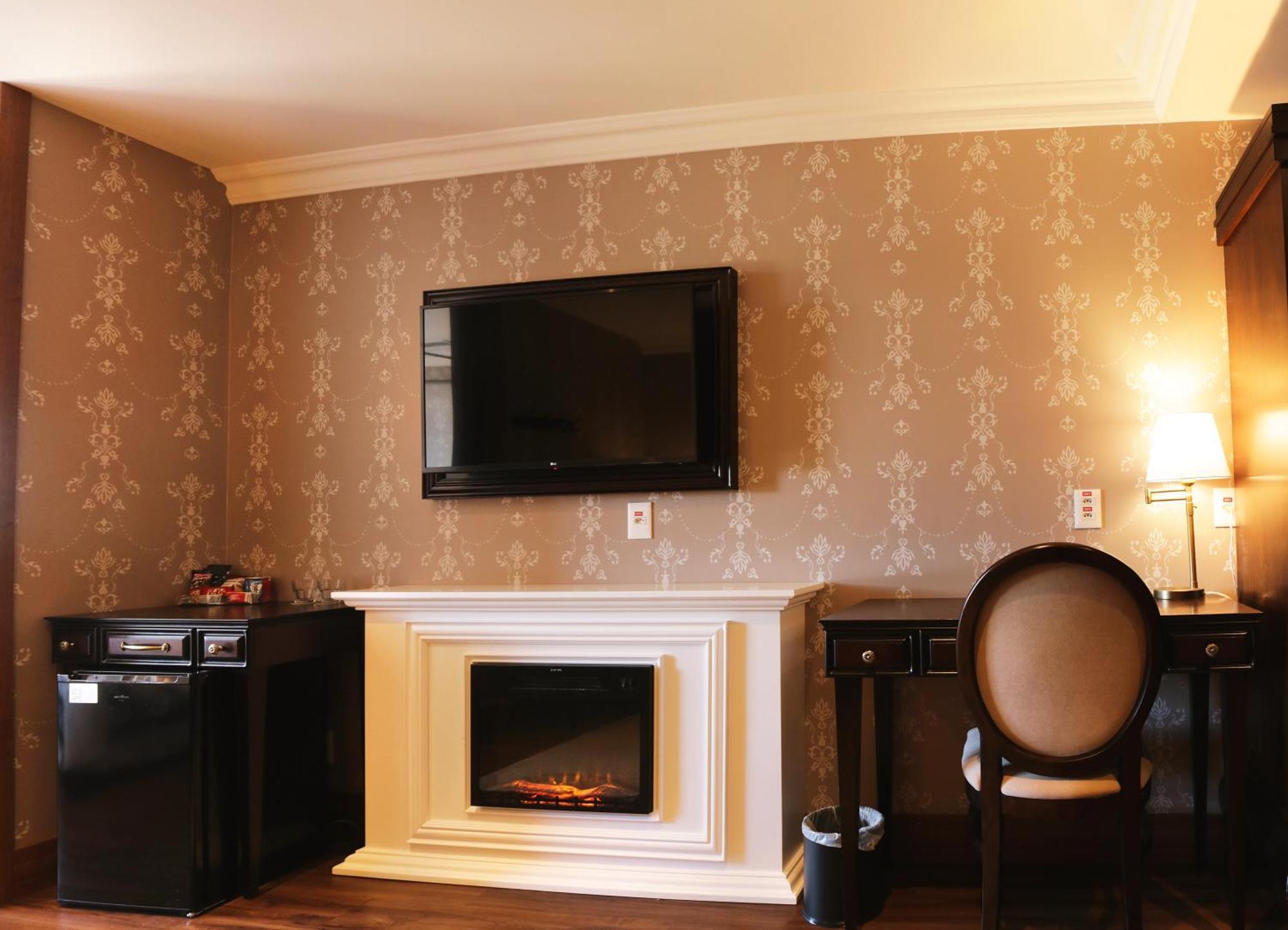 Buona Vitta Gramado Resort & Spa By Gramado Parks Exteriör bild The photo shows a cozy room featuring a decorative wall with a subtle pattern. On one side, there is a modern flat-screen television mounted on the wall. Below it, there is a stylish electric fireplace framed in white. Adjacent to the fireplace is a 