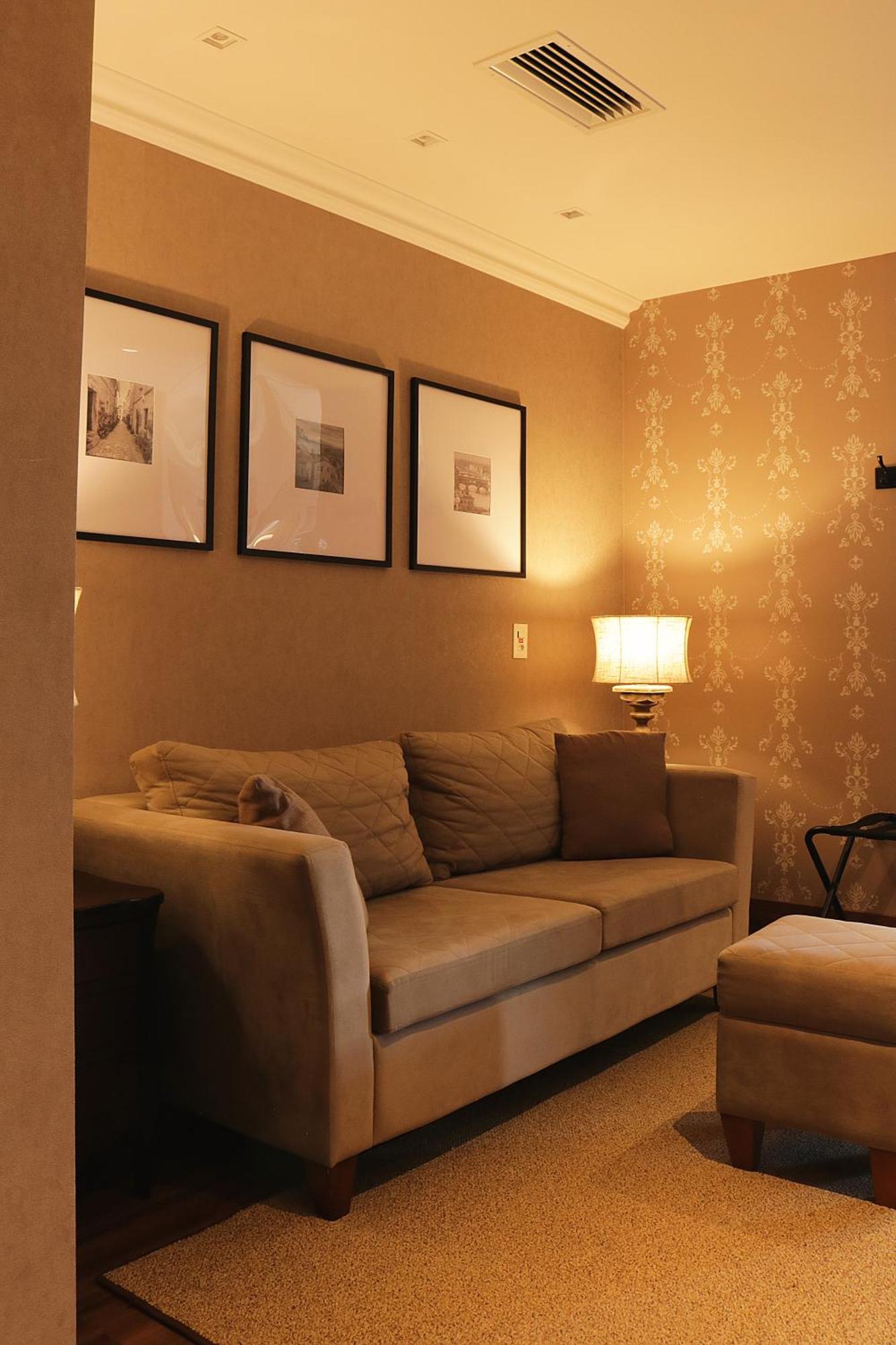 Buona Vitta Gramado Resort & Spa By Gramado Parks Exteriör bild The photo shows a cozy living room setting. There is a light-colored sofa adorned with several cushions, positioned against a wall that has a subtle pattern. Above the sofa, there are three framed artworks or photographs hanging on the wall. To the s