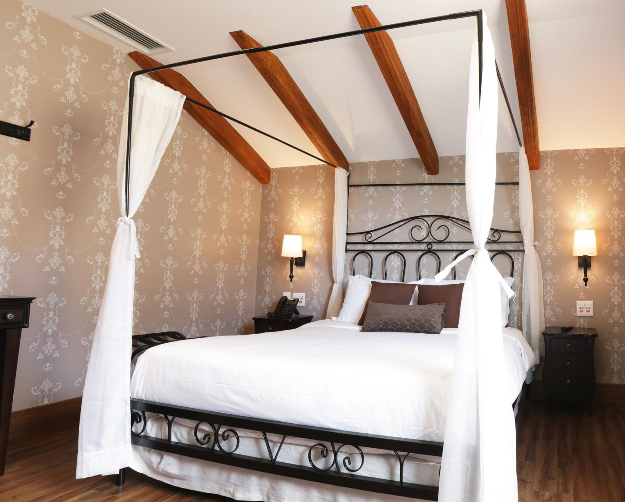 Buona Vitta Gramado Resort & Spa By Gramado Parks Exteriör bild The photo shows a beautifully designed bedroom featuring a four-poster bed with a metal frame and flowing white curtains. The bed is adorned with white bedding and brown decorative pillows. The room has wooden beams on the ceiling and is decorated wi