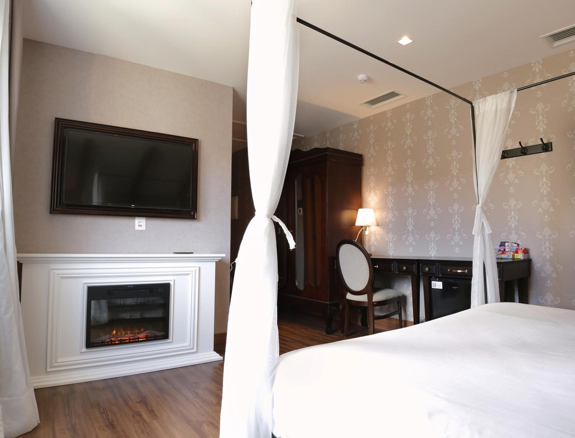 Buona Vitta Gramado Resort & Spa By Gramado Parks Exteriör bild The photo shows a cozy hotel room with elegant decor. There is a white bed with a canopy, and a modern television mounted on the wall across from it. To the side, a fireplace is built into a white mantel, adding a warm touch to the space. There's a w