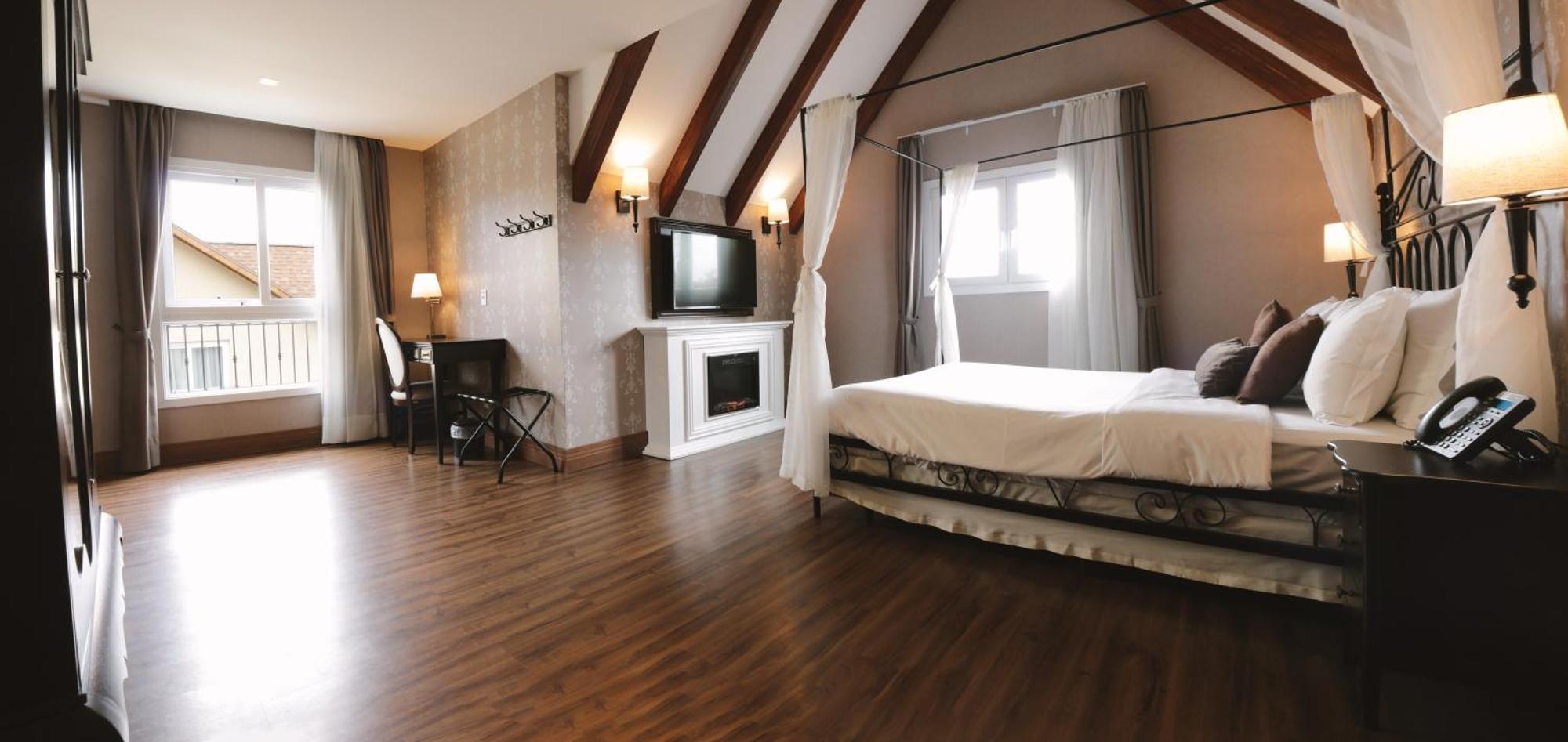 Buona Vitta Gramado Resort & Spa By Gramado Parks Exteriör bild The photo shows a spacious hotel room with a modern and elegant design. There is a large bed with an overhead canopy, and the bed is dressed in white linens. To the side, there is a small seating area with a desk and chair. A flat-screen television i