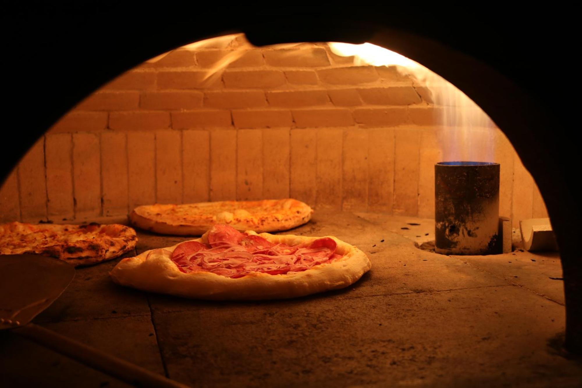 Buona Vitta Gramado Resort & Spa By Gramado Parks Exteriör bild The photo shows a traditional pizza oven. Inside the oven, there are several pizzas placed on the stone surface. The pizzas appear to have various toppings, including what looks like cheese and possibly pepperoni. The oven has a warm, glowing ambianc